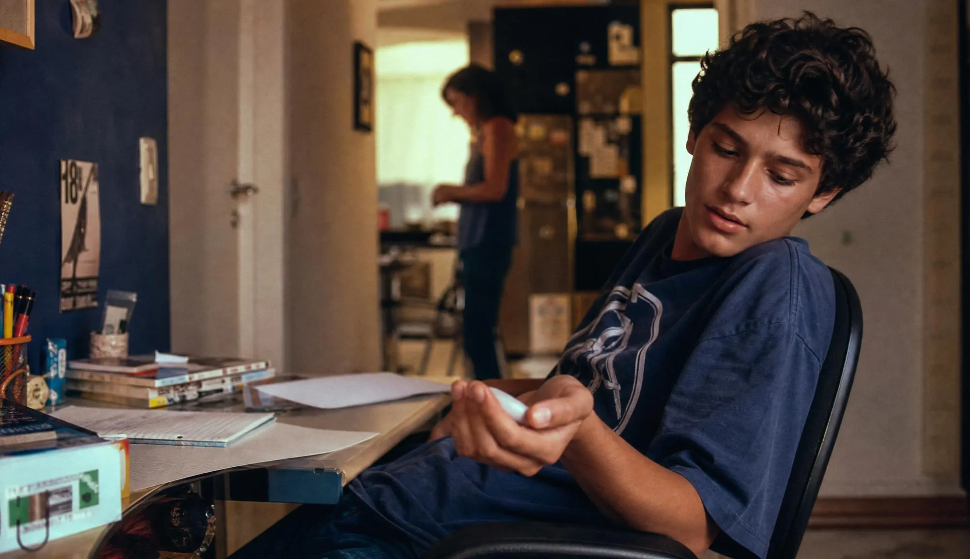 Young person using the device beside schoolwork at a desk.