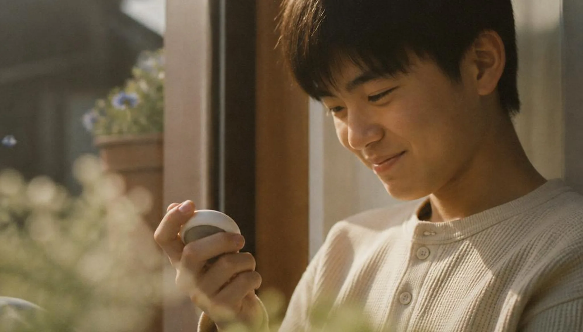 Window-lit portrait of a young person holding the device.